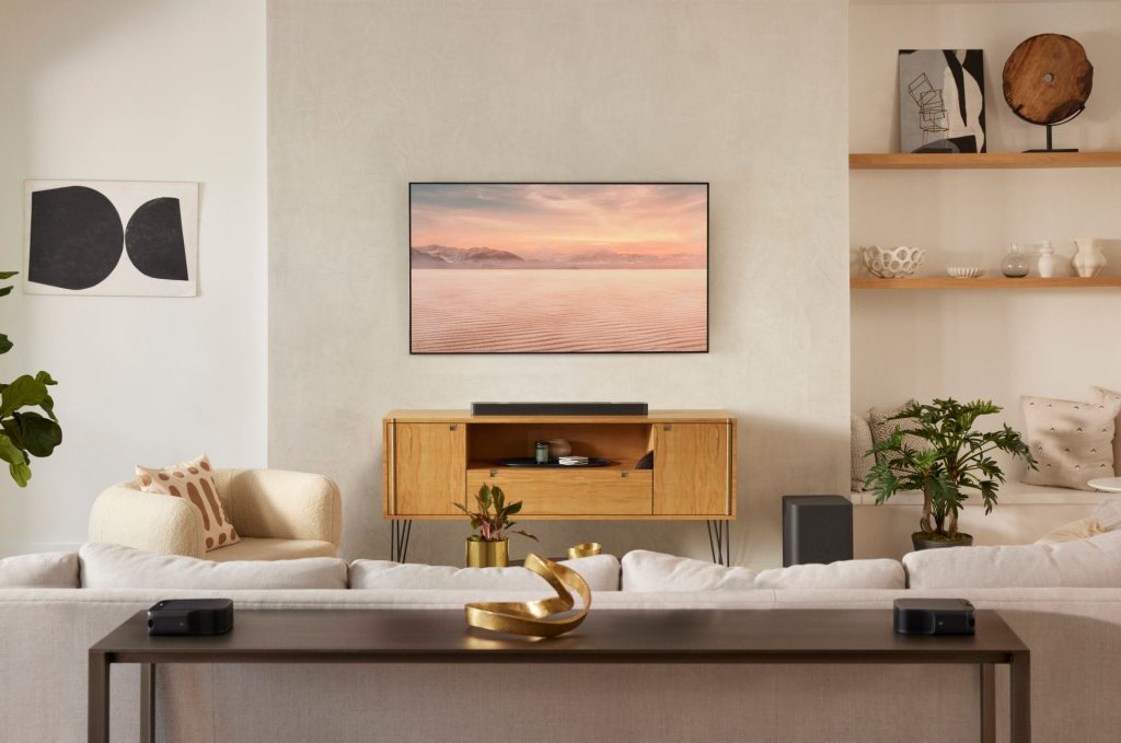 JBL Bar 1000 s umiestnením pod televízorom, na zemi je položený soundbar a v zadnej časti satelitné reproduktory